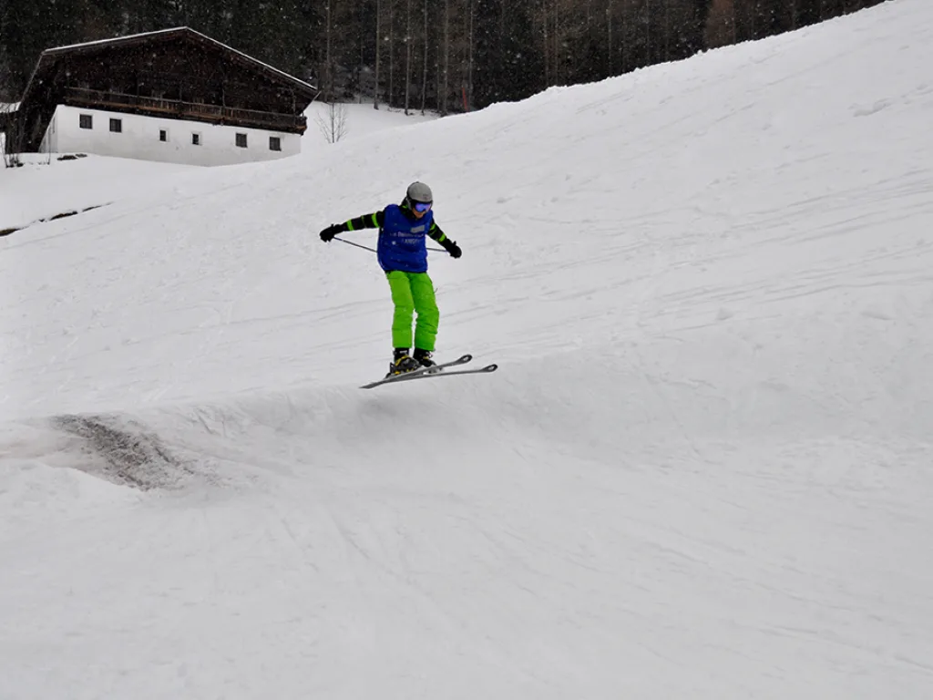 Skifahrer in grüner Hose auf dem Hang vor dem Stadel.